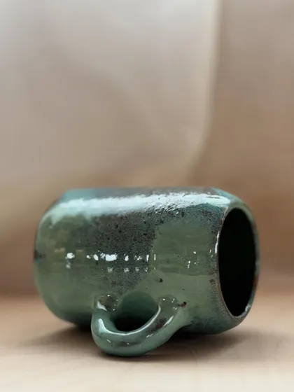 A close-up of a student's mug, showing the beautiful interaction of green and brown glazes. Each piece that comes out of the kiln is a unique surprise.