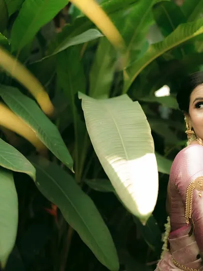 A playful and charming portrait of a bride peeking out from behind tropical leaves.
