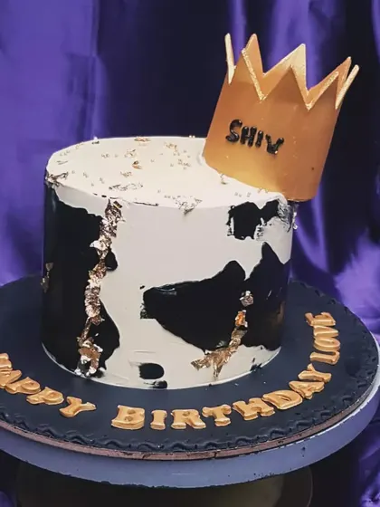 A modern and bold design for a king. This cake features a black and white abstract pattern with gold leaf accents and is topped with a golden crown, making a strong statement for a birthday celebration.