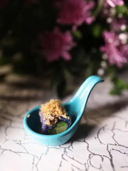 Even a single bite can be a work of art. This piece of our signature purple rice sushi is served on a ceramic spoon, topped with a crunchy crumble for added texture.