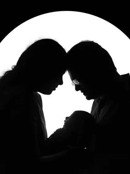 Sometimes, the most powerful family portraits are the simple ones. This silhouette shot creates a timeless and emotional image, focusing on the bond between new parents and their baby against a clean, bright background.