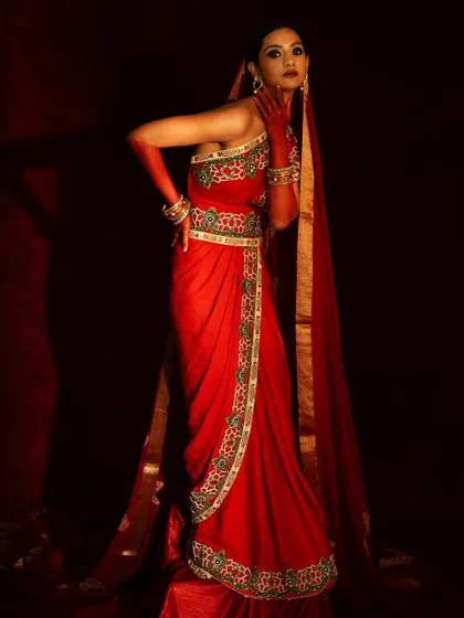 A powerful, full-length standing pose that showcases the elegant drape of the red saree and the long veil.