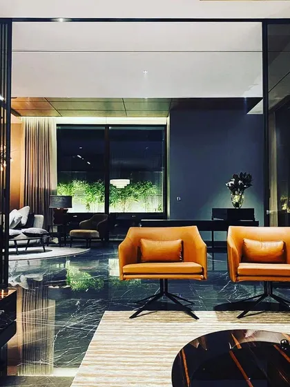 This formal living area in a Palam Vihar residence exudes moody sophistication. The lighting is intentionally kept low and warm, using pools of light from table lamps and accent fixtures to create intimate seating zones against a backdrop of softly lit curtains.