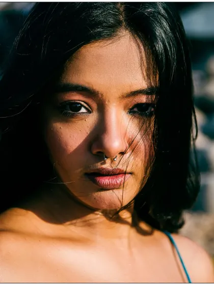 A striking close-up portrait with dramatic, dappled lighting across the model's face. The nose ring adds a touch of modern edge.