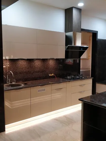 A clean and modern kitchen with beige high-gloss cabinets and a dark granite backsplash and countertop. The under-cabinet lighting provides excellent task illumination.