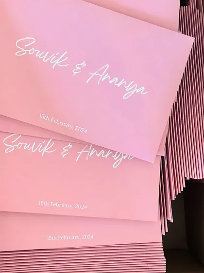 A stack of modern pink envelopes with the couple's names printed in a stylish white script font.