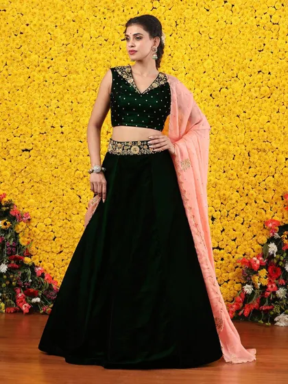 A luxurious dark green velvet lehenga paired with a contrasting soft peach dupatta. The embellished blouse and belt add a touch of sparkle to this elegant ensemble.