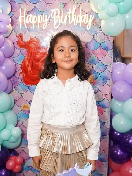 A lovely photo of the birthday girl in front of her mermaid-themed backdrop, featuring pastel balloons and iridescent fish scales.