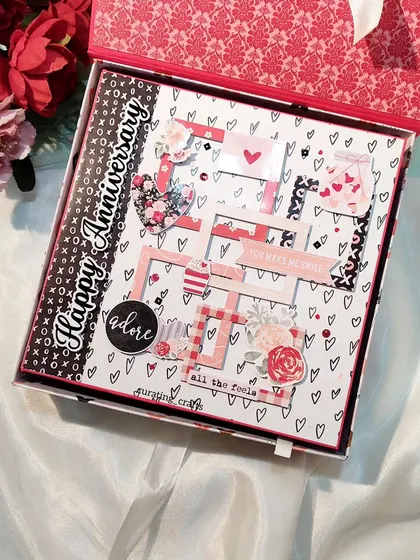 A closer look at the intricate cover of the "Happy Anniversary" scrapbook, with its layered frames and floral embellishments.