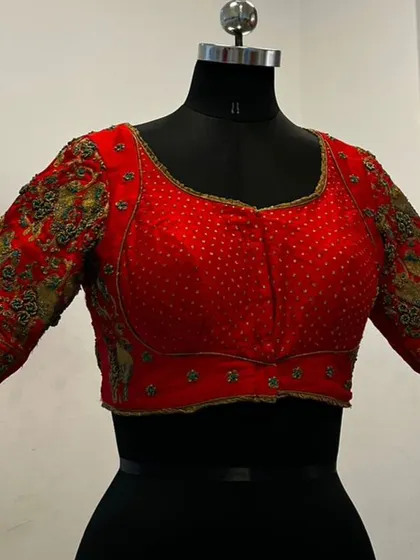 A still image of a vibrant red blouse, showcasing the pearl-like embellishments on the body and the heavy, multi-colored threadwork on the sleeves. This type of detailed craftsmanship is perfect for our rental platform.