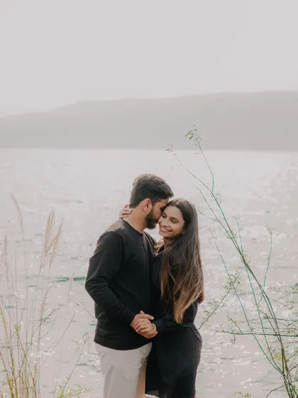 An intimate embrace by the water's edge. The sparkling water and hazy mountains in the background create a dreamy, romantic backdrop for this couple's portrait.