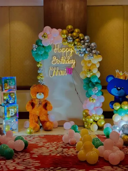 A cute teddy bear themed birthday party. The setup includes a teddy bear prop, 'BABY' blocks, and a balloon arch with a neon sign.