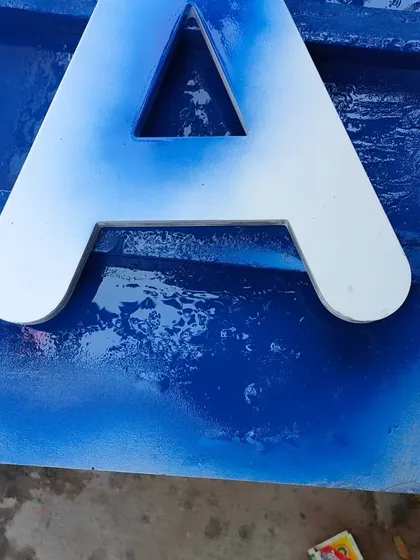 The first coats of blue Duco being applied to a letter 'A'. The spray application builds up the colour gradually, ensuring a deep, rich, and uniform final appearance without any brush marks.