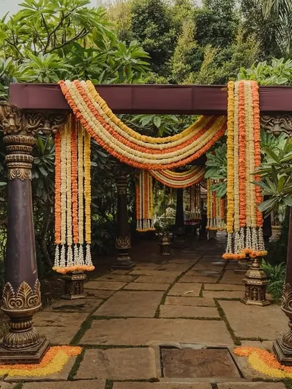 A pathway through a garden framed by traditional pillars and draped with marigold garlands, creating a beautiful walkway for guests.