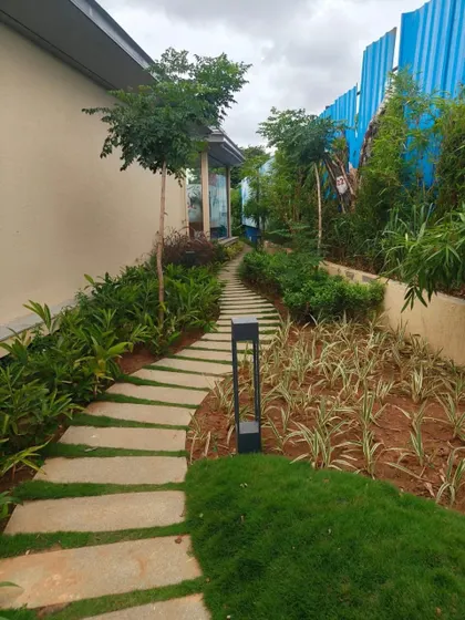 A winding garden path made of stone slabs, leading through a newly planted garden with modern outdoor lighting fixtures.
