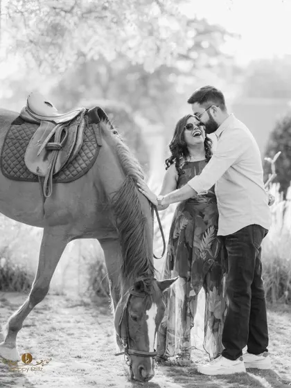 A joyful black and white shot of a couple laughing with a horse. This unique and fun pre-wedding photo shows how we can incorporate different elements to make your shoot special.