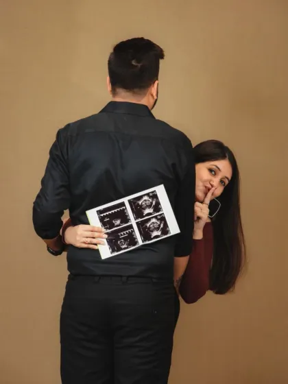A playful and creative announcement photo. The mother-to-be peeks from behind her partner while holding the ultrasound pictures, creating a sense of sweet secrecy and excitement.