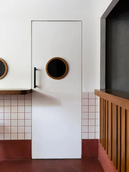 Every detail contributes to the theme, including the doors. A clean white door with a circular, porthole-style window adds a subtle nautical or retro touch, complementing the simple geometry of the tiled walls and wooden counter.