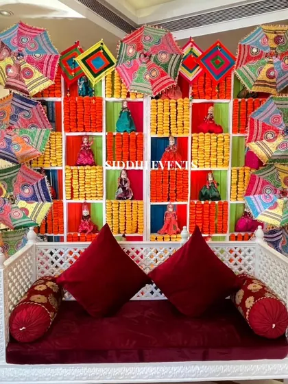 We blended tradition with vibrant elegance in this Haldi seating area. The backdrop features colorful Gujarati umbrellas, marigold garlands, and whimsical Rajasthani kathputli dolls for a culturally rich and festive celebration.