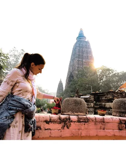 A pilgrim makes an offering near the stupas at the Mahabodhi Temple complex, with the main spire visible in the background. This shot documents the personal and devotional side of a pilgrimage to this holy site.