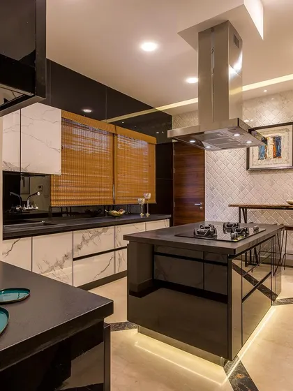A luxurious island kitchen with black and white marble-finish cabinets, a sleek black island with a built-in hob, and a cozy breakfast counter with a raw wooden finish.