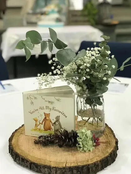 A rustic centerpiece with a wood slice, a small book, and a simple floral arrangement. It's perfect for a woodland or storybook-themed event.