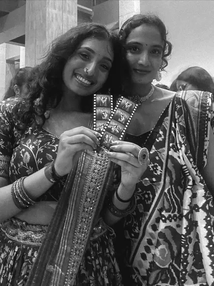 Two friends in beautiful traditional wear at a college event, smiling with their photo strips.