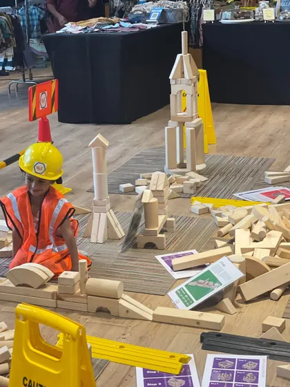 I believe in the power of play, and our dedicated kids' zones are designed for exactly that. Here, a young engineer is completely absorbed in building with giant wooden blocks, an example of the open-ended, creative fun I arrange to keep your children happily engaged.