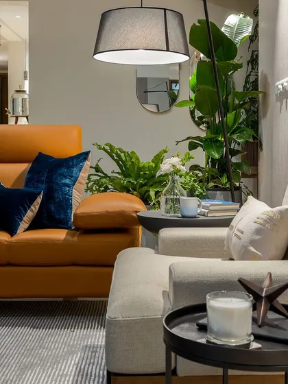 This living space balances sharp geometry with soft curves. A classic tan leather sofa brings warmth, while pops of royal blue and lush indoor plants add vibrancy and soften the modern design.
