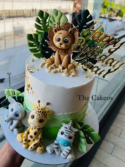 A jungle safari cake with a fondant lion on top and an elephant, giraffe, and zebra at the base, ready for a wild celebration.
