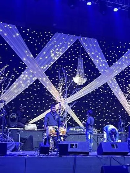 A sangeet stage designed for a live band, with a "starry night" backdrop of fairy lights, crisscrossing white drapes, and illuminated tree props.