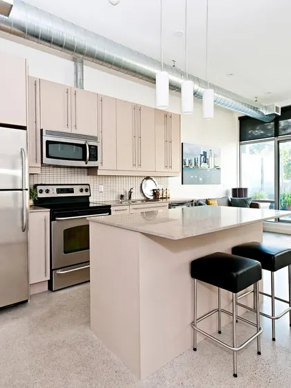 An open-plan kitchen with a compact island, perfect for smaller apartments. The light-colored cabinets and stainless steel appliances create a bright and functional cooking space that connects seamlessly with the living area.