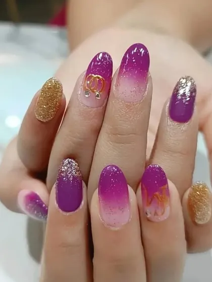 A vibrant purple ombre set with gold glitter accent nails and a delicate, dangling heart charm.