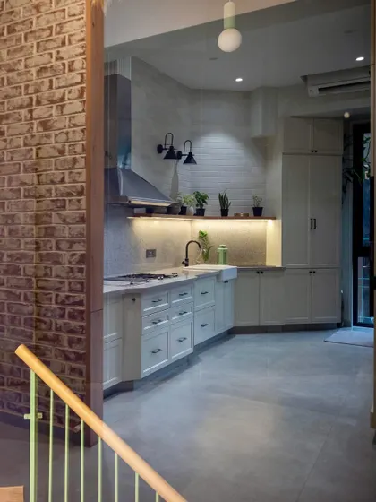 This open and airy kitchen uses white cabinetry and exposed brick to create a rustic yet modern feel. The layout is designed to be a living kitchen, integrated with the rest of the home.