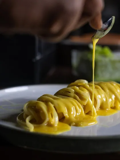 A chef carefully drizzles the creamy yuzu butter sauce over a twirl of linguine. This action shot highlights the care and precision that goes into plating my pasta dishes.