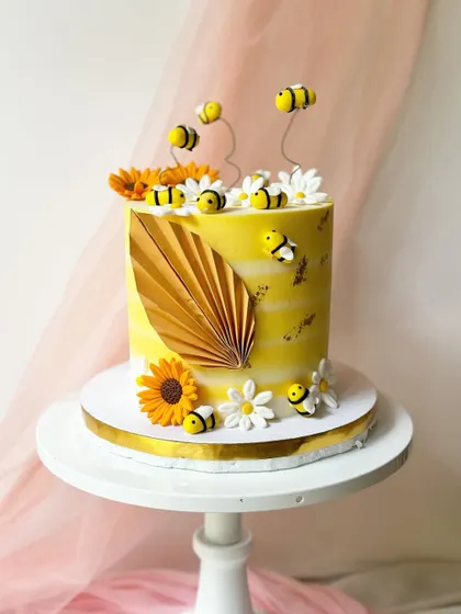 A cheerful bee-themed cake that's buzzing with detail. The yellow watercolour buttercream is decorated with fondant sunflowers, daisies, and lots of cute little bees.