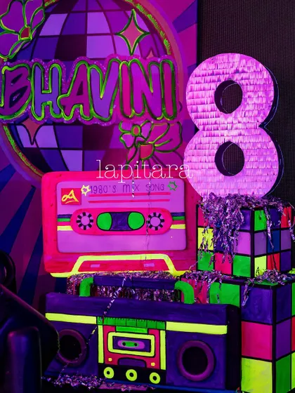 A retro decor piece for a neon party, featuring a cassette tape, a Rubik's cube, and a piñata shaped like the number 8.
