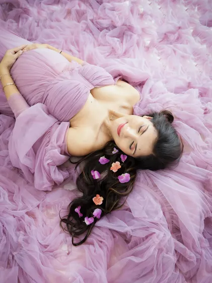 A dreamy overhead shot of a mom-to-be lying in a sea of lavender tulle, with delicate flowers in her hair. A truly artistic and beautiful portrait.