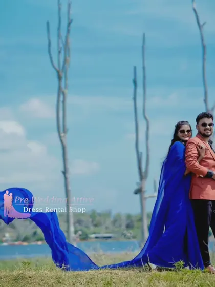 A couple enjoys a lakeside view. The woman wears a blue trail saree, and the man is in a complementary colored jacket, creating a relaxed yet stylish look.