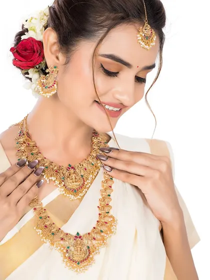 A close-up of the model adjusting her traditional necklace, offering a detailed view of the multi-colored stones and intricate design.