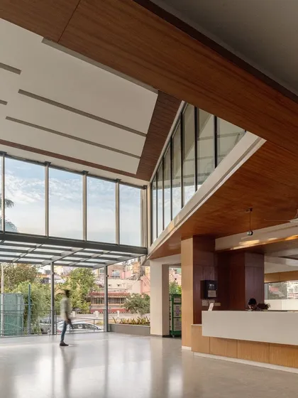 The reception lobby of the Koramangala Club Annexe is a light-filled, double-height space that overlooks the club's grounds. The expansive glazing and clean lines create a welcoming and spacious atmosphere for members and guests.