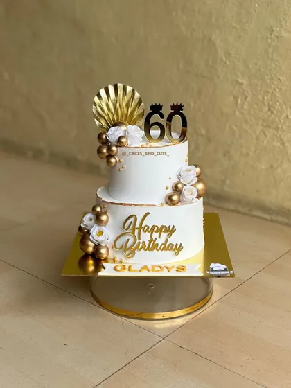 A glamorous two-tier cake for a 60th birthday, decorated in white and gold with floral and balloon accents. We cover how to create elegant designs for milestone birthdays.