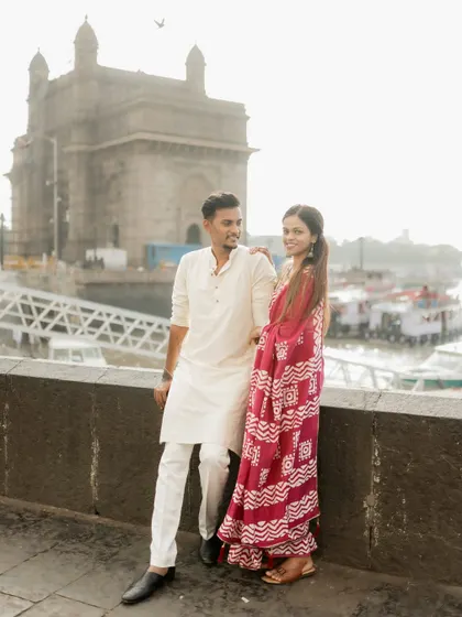A classic pre-wedding portrait of the couple standing together with the Gateway of India in the background, showcasing their traditional outfits and the iconic Mumbai location.