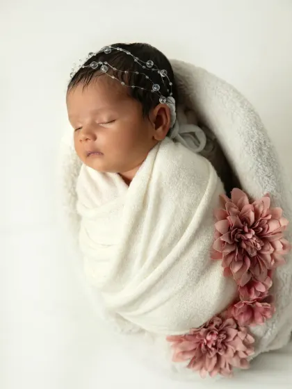 A full view of the baby wrapped in a soft white blanket, adorned with pink flowers. This classic pose is always a favorite among parents.
