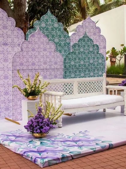 A minimal yet striking Moroccan-inspired Mehendi stage. The custom-printed backdrops and flooring, paired with a simple white bench and purple floral accents, create a chic and modern look.