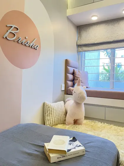 A close-up of the cozy corner in the kid's room, with a pink unicorn plushie sitting by the bay window seat. The color-blocked wall with a custom nameplate adds a personal touch.