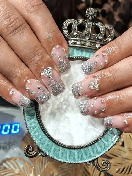 "Glass slipper" style nails featuring a sheer base with silver glitter and crystal accents, finished with a crown-themed holder.