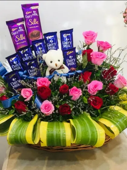 A slightly different angle of the chocolate and flower gift basket. This view shows how the teddy bear is nestled among the pink and red roses and Dairy Milk bars.
