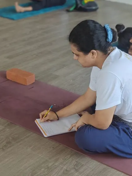 The path to becoming a teacher involves being a dedicated student first. Here, a student diligently takes notes during a lecture, absorbing the theoretical aspects of yoga.