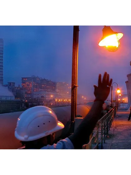 A shot capturing workers at a power plant during dusk. The composition uses the warm glow of an industrial lamp to highlight the human presence and scale of the environment.
